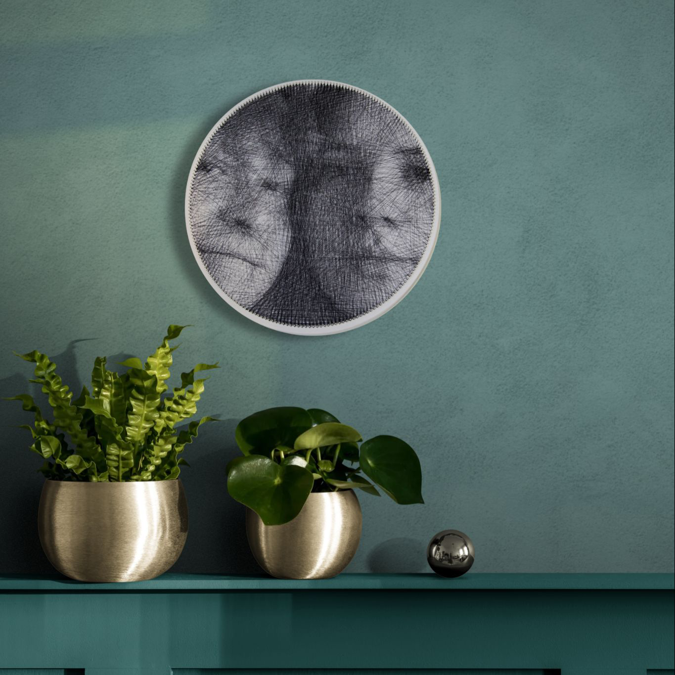 Round black string art portrait mounted on a muted green wall above a cabinet with potted plants.