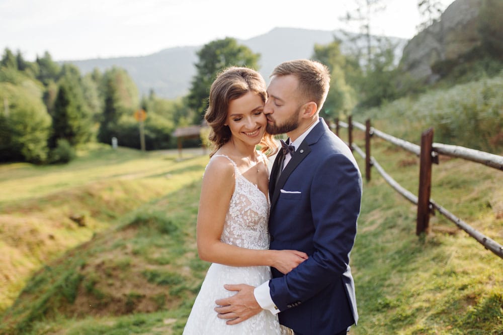Bride and groom standing close together outdoors in a natural landscape, smiling and embracing during a wedding photo session.