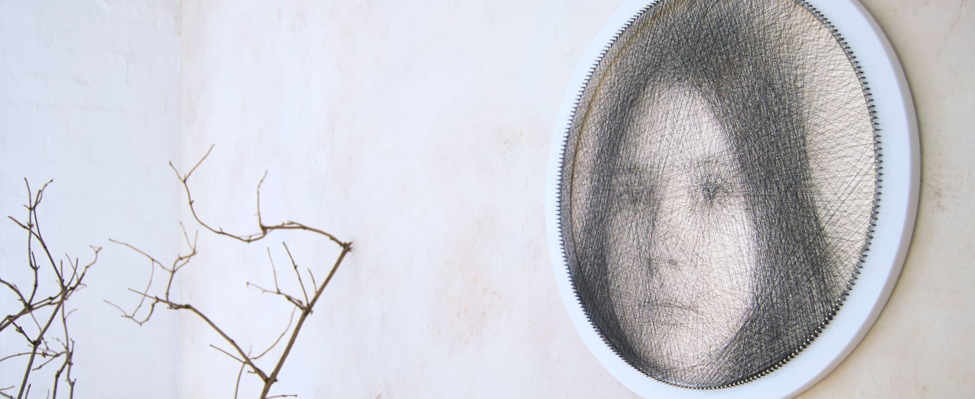Ring string art portrait on a white wall, created with black thread on a closed round wooden base.