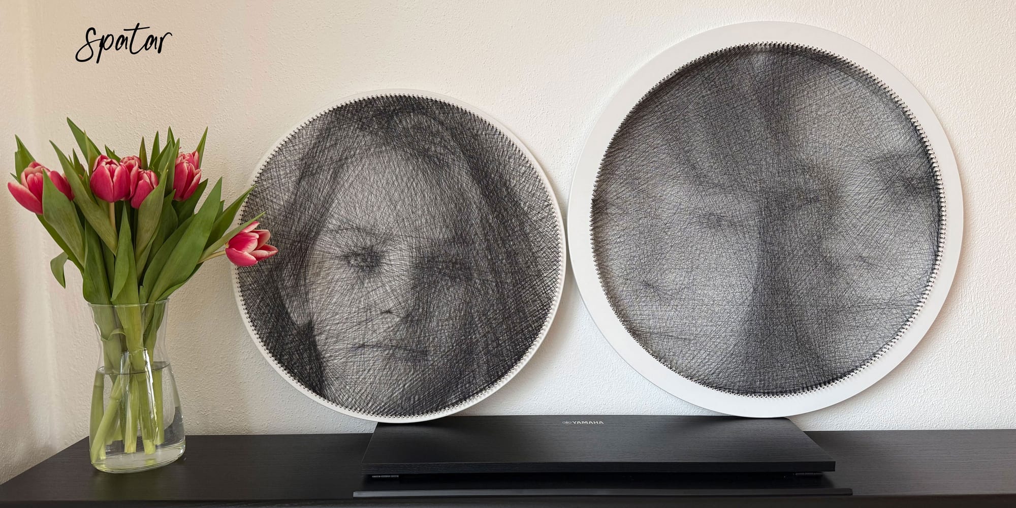 Pair of round string art portraits on shelf next to vase of tulips