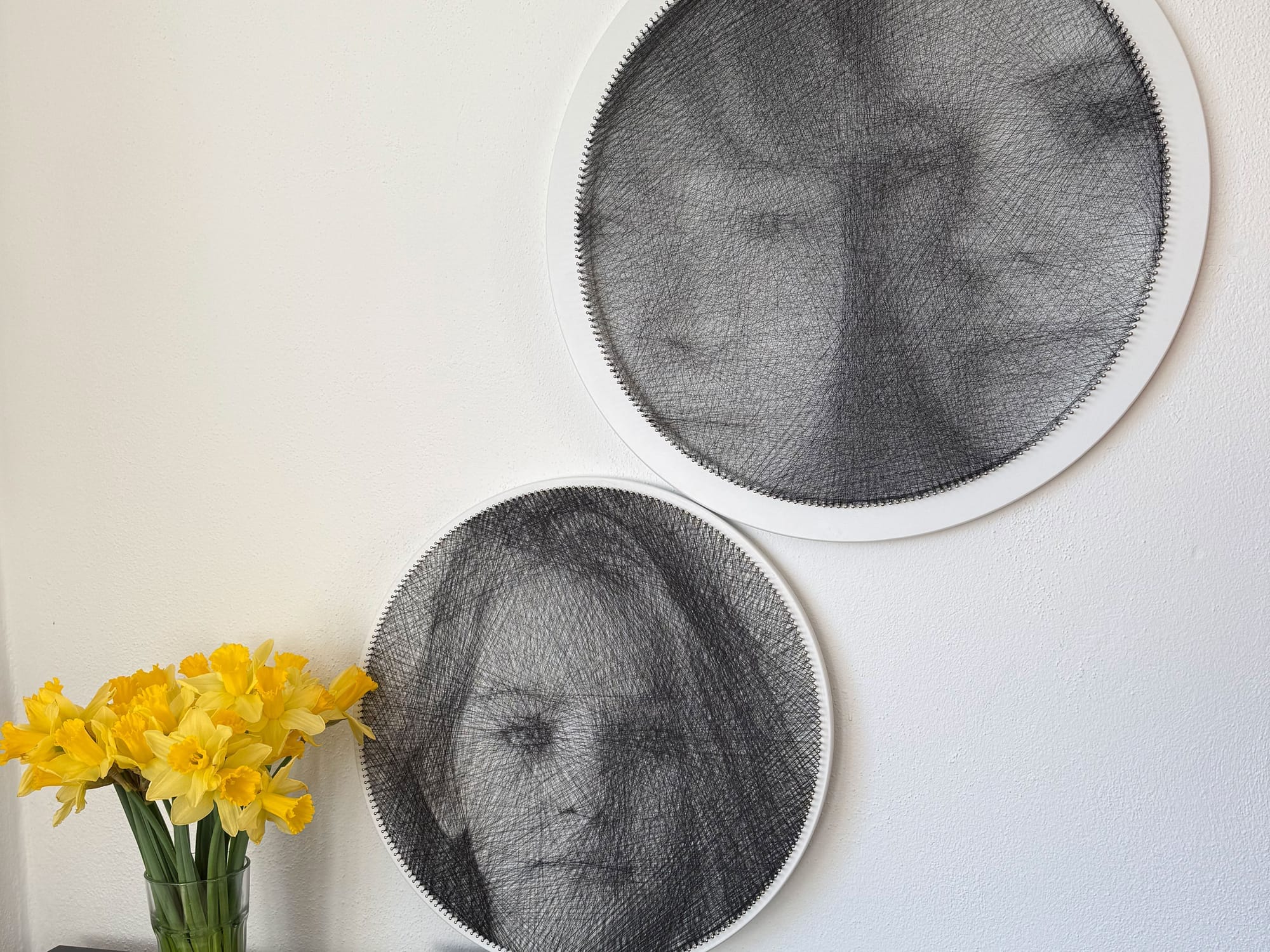 Deux portraits personnalisés en string art terminés accrochés à un mur