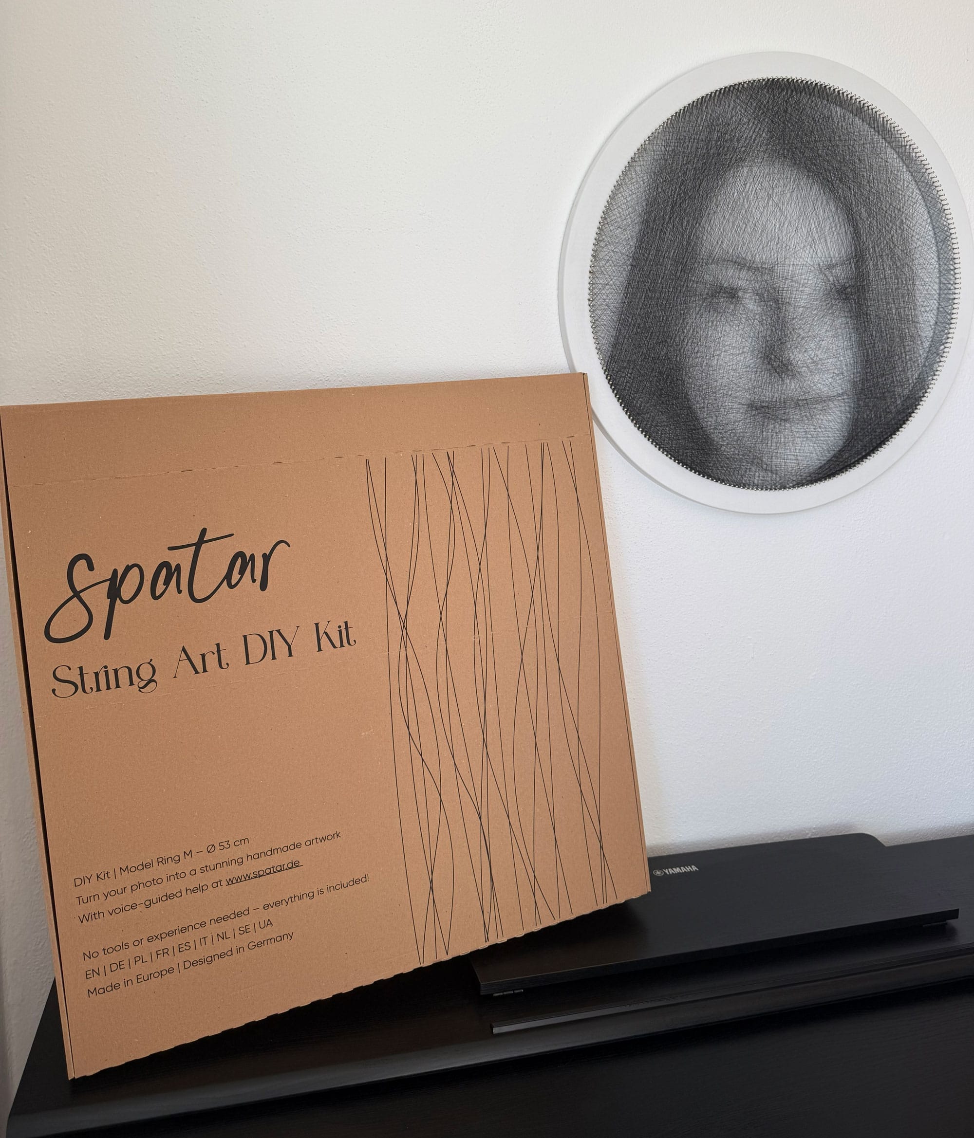 Kit DIY Spatar à côté d’un portrait en string art terminé